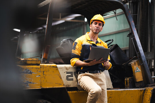 warehouse worker working on laptop computer : Hispanic latin man staff driving forklift in industrial container factory warehouse. Worker communicate by walkie talkie transmitter, radio
