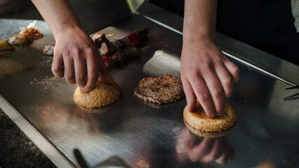 Hands grilling burger buns and patty on a teppanyaki grill