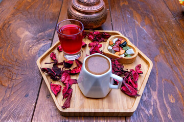 Traditional Turkish coffee served with rose petals, nuts, and a glass of tea on a wooden tray, showcasing authentic Middle Eastern hospitality and rich cultural flavors.