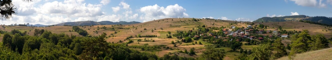Obraz premium A panoramic view of Kurtlu Village in Boyabat, Sinop, showcasing lush green hills, scattered houses, and a peaceful rural landscape under a partly cloudy sky.