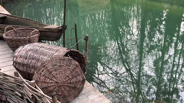 Antique wooden fishing boat and wicker fish baskets on the lake shore.