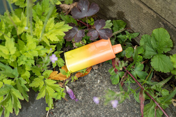 A discarded electronic cigarette vape that has been left behind in some weeds on a concrete path.