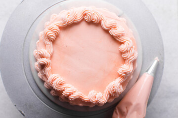 piping border on Pink buttercream cake on a cake plate, Cake covered in pink frosting, process of decorating top of cake with pink buttercream