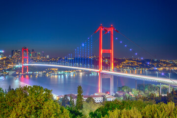 Brightly illuminated 15 july martyrs bridge at night, spanning bosphorus with glowing red towers and blue lights, reflecting on calm water, showcasing istanbul’s vibrant cityscape Turkiye Turkey best
