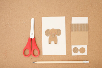 Cardboard elephant made from cut paper shapes on white sheet with scissors, pencil, and paper...
