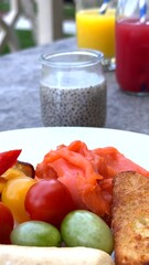 Cured meat lies beside cherry tomato, juicy grapes, sausages, bread cubes, juice and chia glass on sunlit table, offering rustic contrast at elegant tourist destination breakfast.