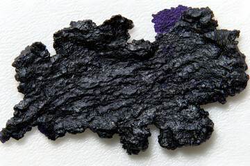 Abstract close-up of a dark, textured substance resembling dried paint or ink blot, exhibiting a unique organic form with irregular edges and subtle color variations.