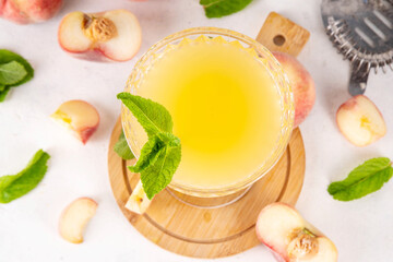 Flat peach martini or margarita lemonade cold fruit drink, summer iced fruit juice cocktail with mint and lemon, on white table