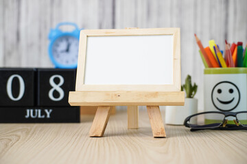 Blank White Board for Chalk Notes On Wooden Desk with Various Stationery Items and Wooden Calendar at the date July 18. Mock up Template for Your Design Write Your To-Do List On July 18