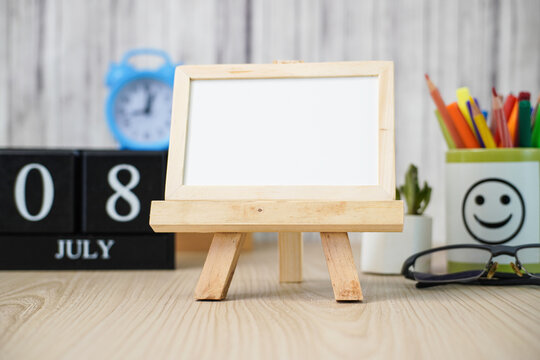 Blank White Board for Chalk Notes On Wooden Desk with Various Stationery Items and Wooden Calendar at the date July 18. Mock up Template for Your Design Write Your To-Do List On July 18