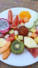 White ceramic plate presenting colorful tropical fruit medley watermelon, kiwi, pineapple, grapefruit, dragon fruit, showcasing fresh, nutritious breakfast arrangement
