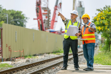 Two male construction engineers wea safety helmets and reflective vests discussing construction...