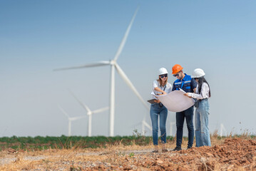 Three engineer people are standing in a field, looking at a large wind turbine