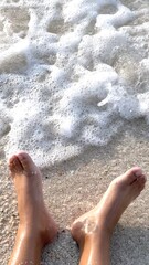 Feet resting on sunlit sea shore, soft waves swirl over skin, sea foam melts into sand, moment captures barefoot freedom, tranquil coastal rhythm invites quiet eco escape and tourist attraction.