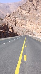 Serpentine asphalt highway cutting through barren uae mountainscape, yellow white lines dividing stark rocky terrain and expansive desert landscape