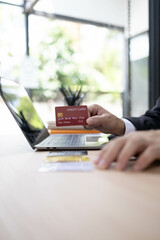 A man is using a laptop and a cell phone to pay for something. He is holding a credit card and a debit card
