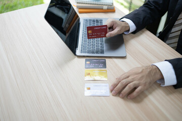 A man is using a laptop and a cell phone to pay for something. He is holding a credit card and a debit card

