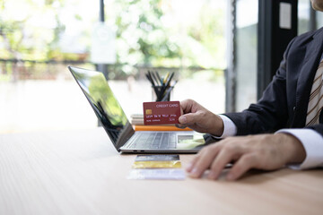 A man is using a laptop and a cell phone to pay for something. He is holding a credit card and a debit card
