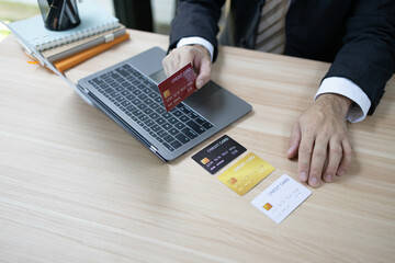 A man is using a laptop and a cell phone to pay for something. He is holding a credit card and a debit card

