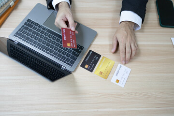A man is using a laptop and a cell phone to pay for something. He is holding a credit card and a debit card
