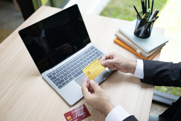 A man is using a laptop and a cell phone to pay for something. He is holding a credit card and a debit card

