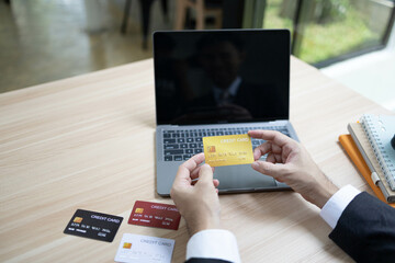 A man is using a laptop and a cell phone to pay for something. He is holding a credit card and a debit card
