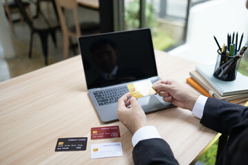 A man is using a laptop and a cell phone to pay for something. He is holding a credit card and a debit card
