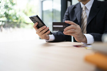 A man is using a laptop and a cell phone to pay for something. He is holding a credit card and a debit card
