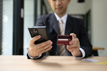 A man is using a laptop and a cell phone to pay for something. He is holding a credit card and a debit card
