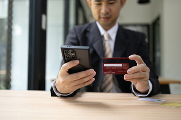 A man is using a laptop and a cell phone to pay for something. He is holding a credit card and a debit card
