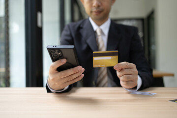 A man is using a laptop and a cell phone to pay for something. He is holding a credit card and a debit card
