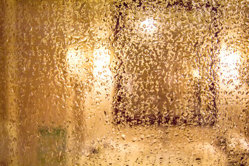 a close-up of a window covered with water droplets, creating a warm and cozy atmosphere perfect for rainy days, introspection, and moody weather themes