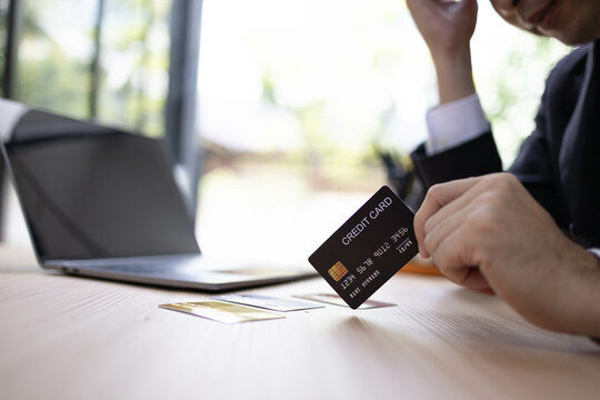 A man is using a laptop and a cell phone to pay for something. He is holding a credit card and a debit card

