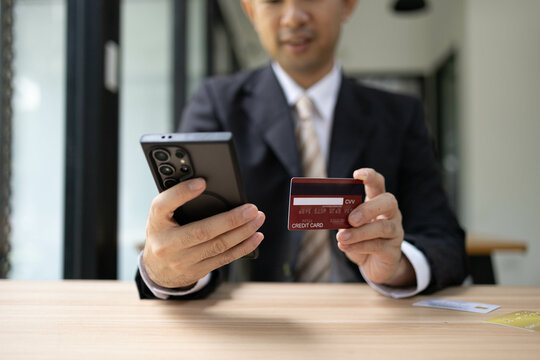 A man is using a laptop and a cell phone to pay for something. He is holding a credit card and a debit card
