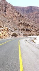 Road wraps desert cliff, distant lights align curve, jagged red hills under bright sky outline modern infrastructure in wild land. Urban isolation concept.