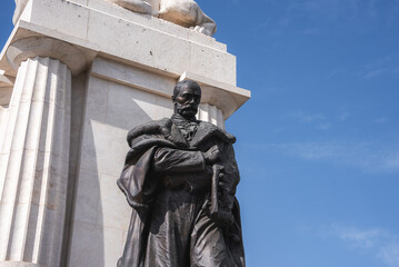 Obraz premium The Tisza Istvan Memorial. A bronze statue of a man in formal attire holding a scroll stands on a white stone pedestal with fluted columns and a sculpted lion in Budapest, Hungary.