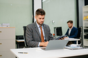 Confident businessman working on finance analysis with a tablet and laptop at office desk