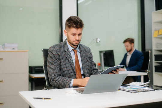 Confident businessman working on finance analysis with a tablet and laptop at office desk