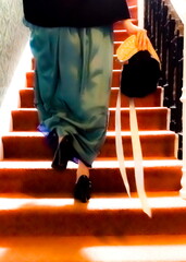 A person in a long dress and holding a hat and fan descends a staircase.