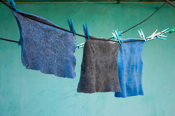 Cloth pieces in shades of blue and gray are hung out to dry on a clothesline, with a bright green...