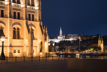 Obraz premium Illuminated Hungarian Parliament Building, Matthias Church, and Fisherman's Bastion at night, with the Danube River and reflections enhancing the scene.