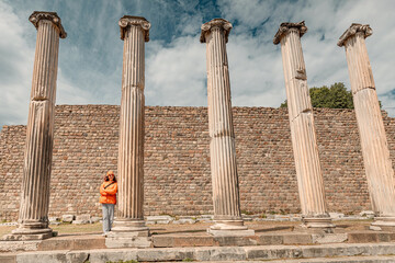 Tourist standing between roman columns in archaeological site, posing for a picture in front of a brick wall