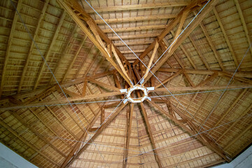 Interior view of a wooden roof structure with radial beams and natural thatch or bamboo covering, showcasing traditional construction techniques and rustic architectural craftsmanship.