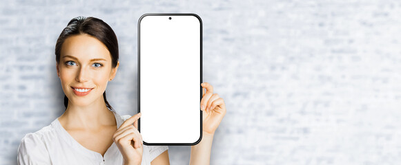 Portrait image - happy smile cute businesswoman business woman show point big mockup cell phone, smartphone mobile cellphone with white screen. Online offer ad. Free text space. Bricks wall background