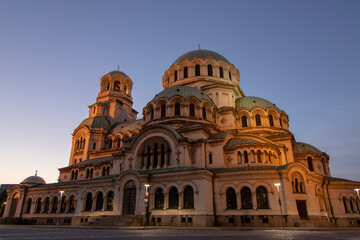 Obraz premium Alexander Nevsky Cathedral in Sofia illuminated by warm sunset light, highlighting its impressive Neo-Byzantine architecture and intricate domes against a clear evening sky.