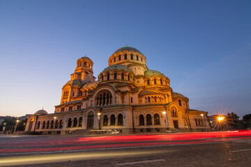 A stunning evening view of Alexander Nevsky Cathedral in Sofia with dynamic light trails from passing traffic, showcasing the majestic Neo-Byzantine architecture against a clear twilight sky.