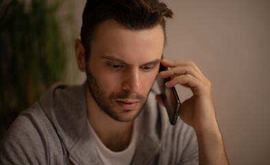 Young man in casual hoodie having a serious phone conversation indoors, focused and concerned, in a...