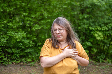 Middle aged woman holding chest in pain, sudden cardiac symptom, heart discomfort, possible rare cardiac condition, health risk