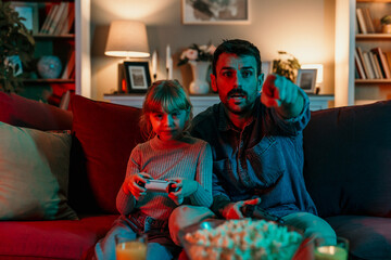 Father and daughter playing videogames with dramatic lighting on sofa
