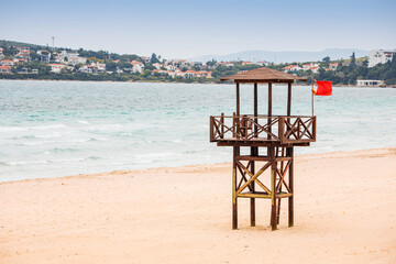 Wooden lifeguard tower stands on a deserted sandy beach with a red flag waving, indicating danger for swimming